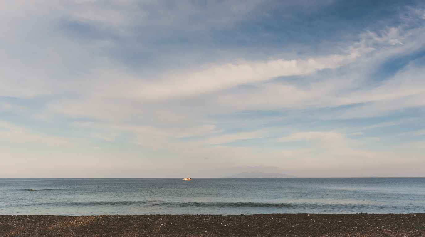 Calm early morning sea at Exo Gialos beach near Fira with a fishing boat on the horizon