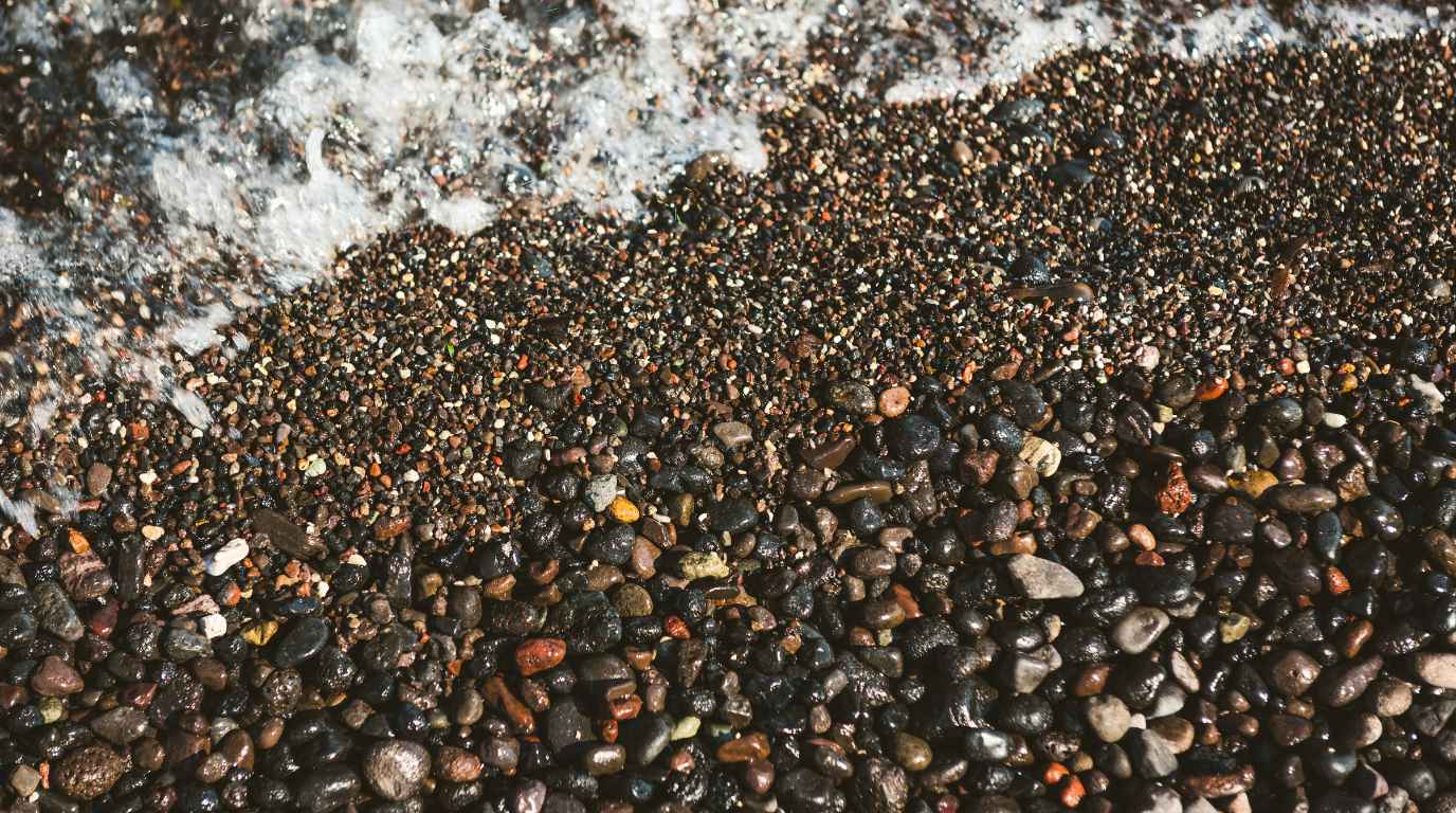 Close-up of smooth black and red volcanic pebbles at the waterline on a Santorini beach