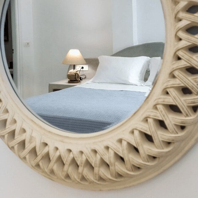 Round woven mirror reflecting the bed in a Standard Suite