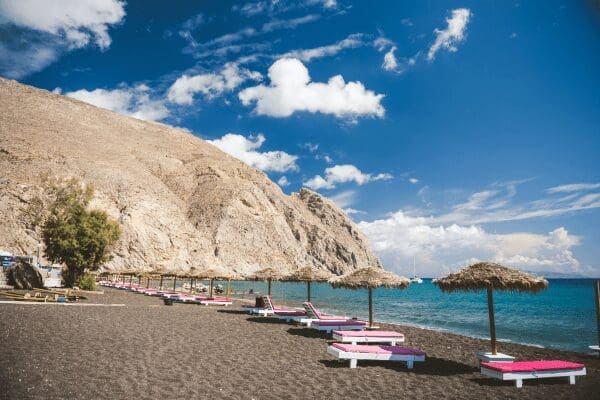Organised black-sand beach at Perissa with straw umbrellas and sunbeds, Santorini