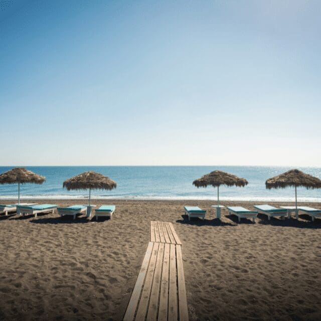 Black-sand beach with straw umbrellas and a boardwalk leading to the sea, Santorini